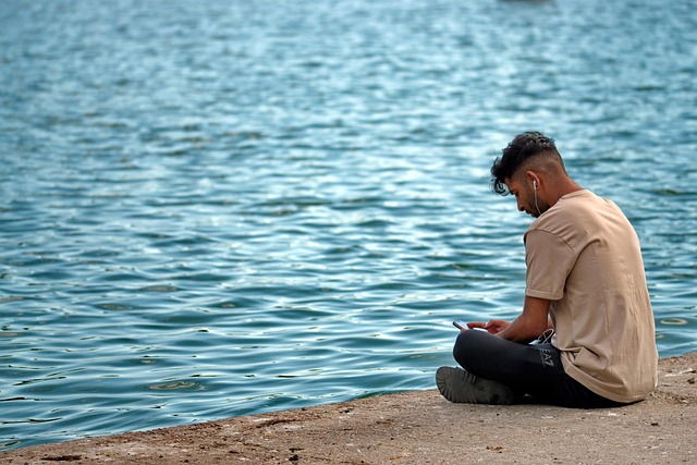 ragazzo seduto davanti al mare distratto dallo smartphone